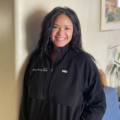 Female dentist in black jacket smiling at camera in modern office setting with plants.