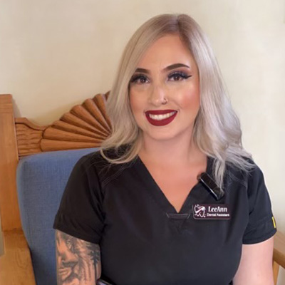 Professional woman with platinum blonde hair wearing black dental office scrubs, smiling at camera indoors.